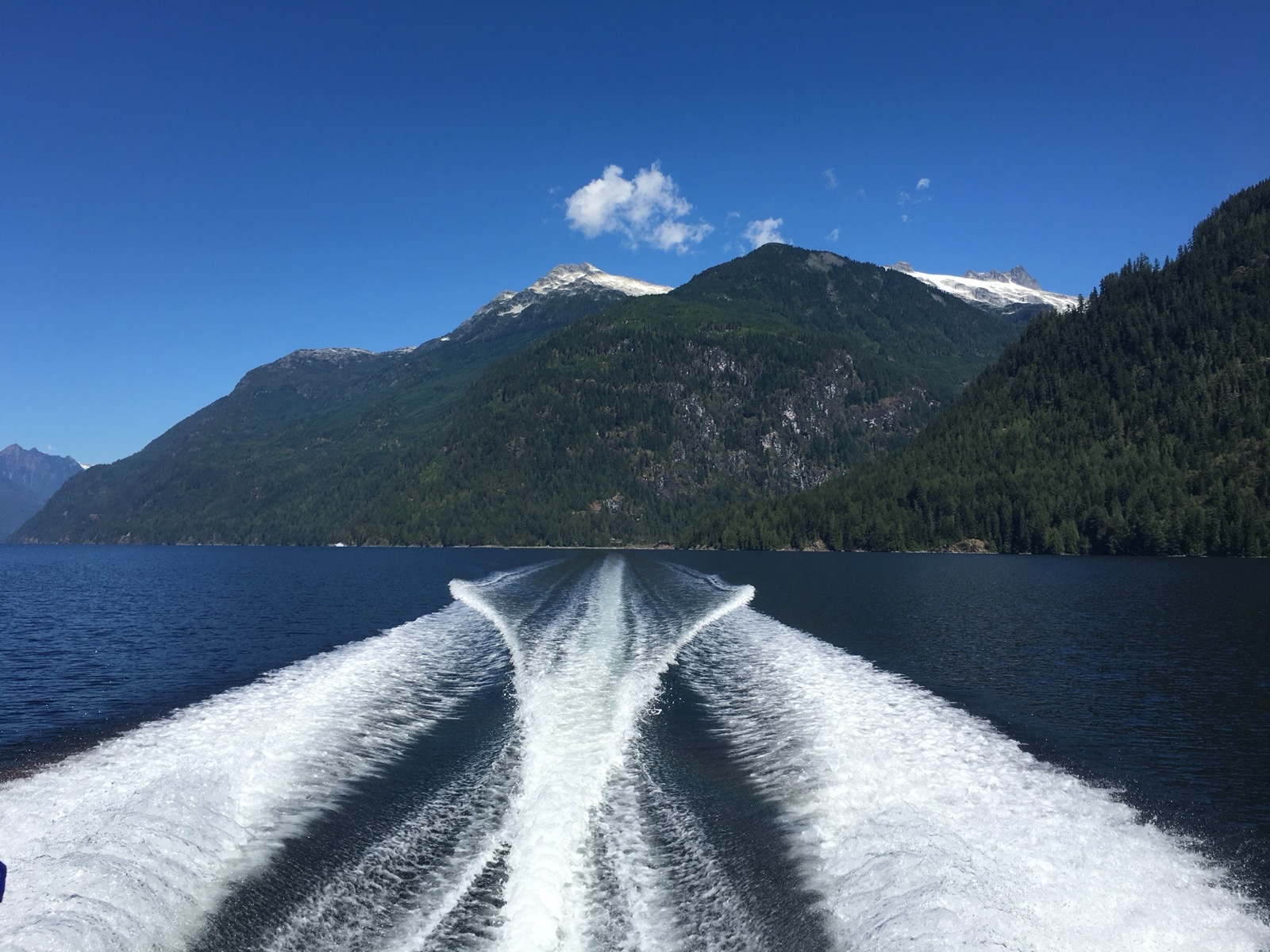The wake of a 23ft Mirage running down a steep-walled inlet under clear sky, snow still on the peaks above the treeline.